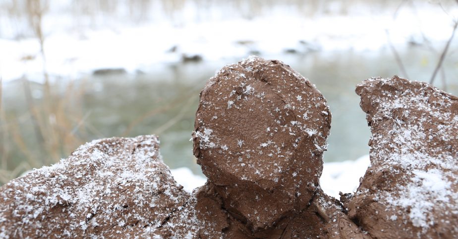 Photograph of a winter scene by a creek, sculpture of frozen clay with snowflakes on top.